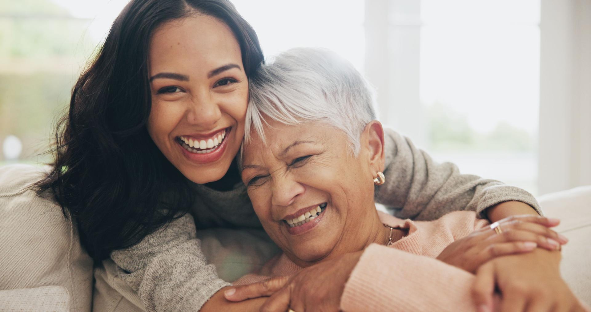 Hug, portrait and smile of old woman with daughter on sofa in living room of home for bonding or visit. Face, family or love with happy person and senior mother embracing in apartment together